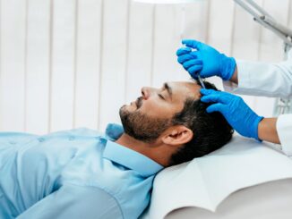 Ein Mann liegt auf einer Behandlungsliege, während eine medizinische Fachkraft mit Handschuhen eine Injektion in die Kopfhaut durchführt.